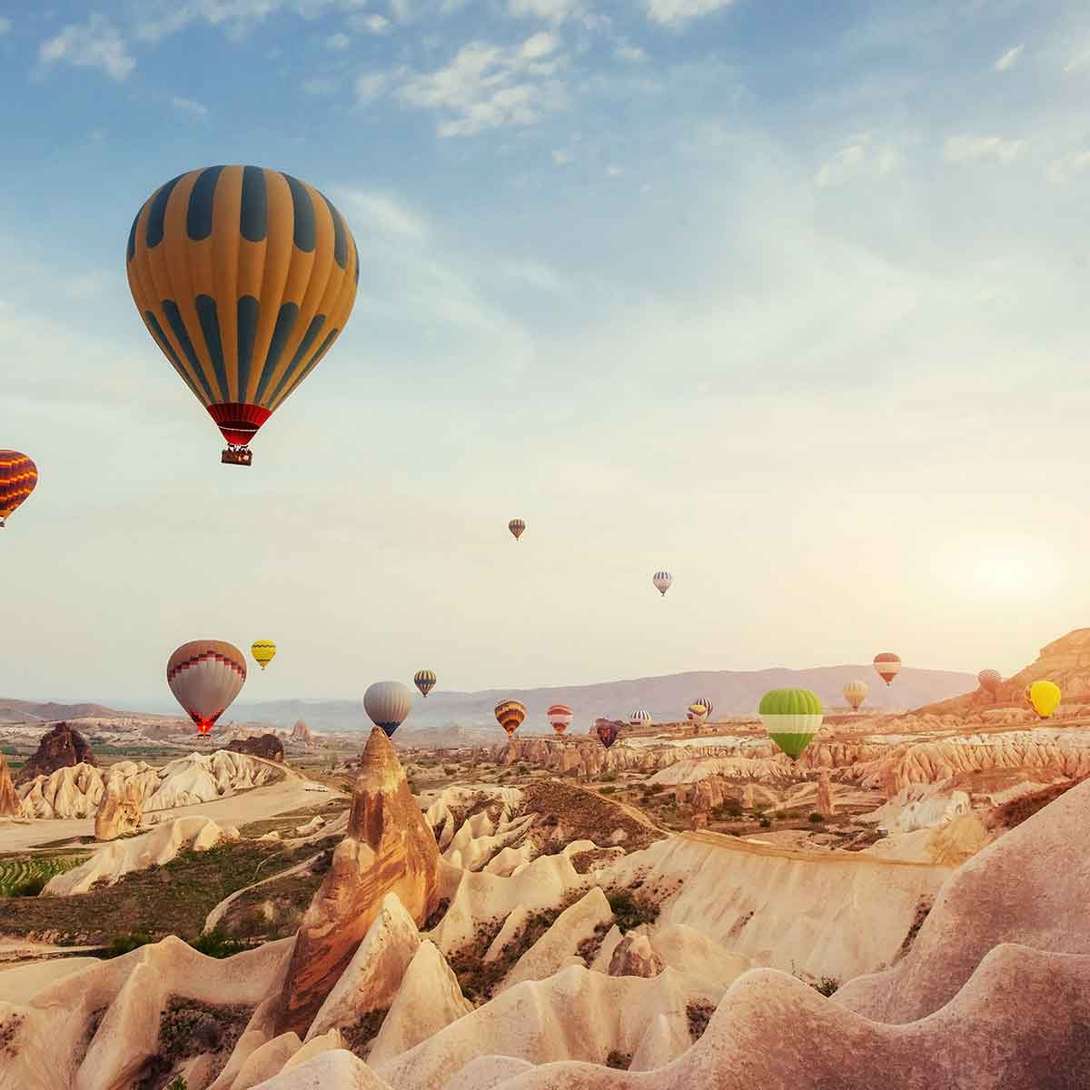 Colorful hot air balloons soaring over Cappadocia's unique rock formations during sunset.
