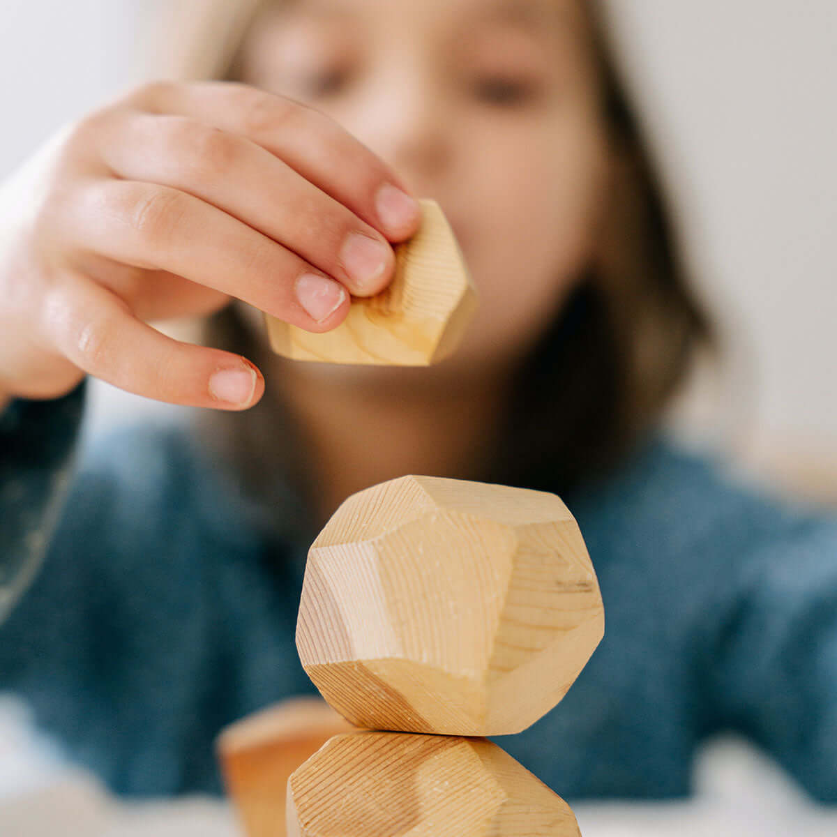 Child stacking wooden geometric blocks, representing learning and play in sustainability education.