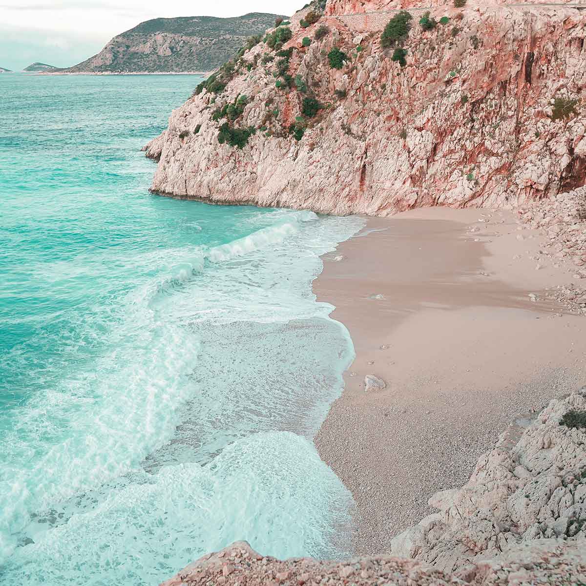 Stunning view of a tranquil beach with turquoise water and rocky cliffs in Antalya, showcasing the Mediterranean paradise.