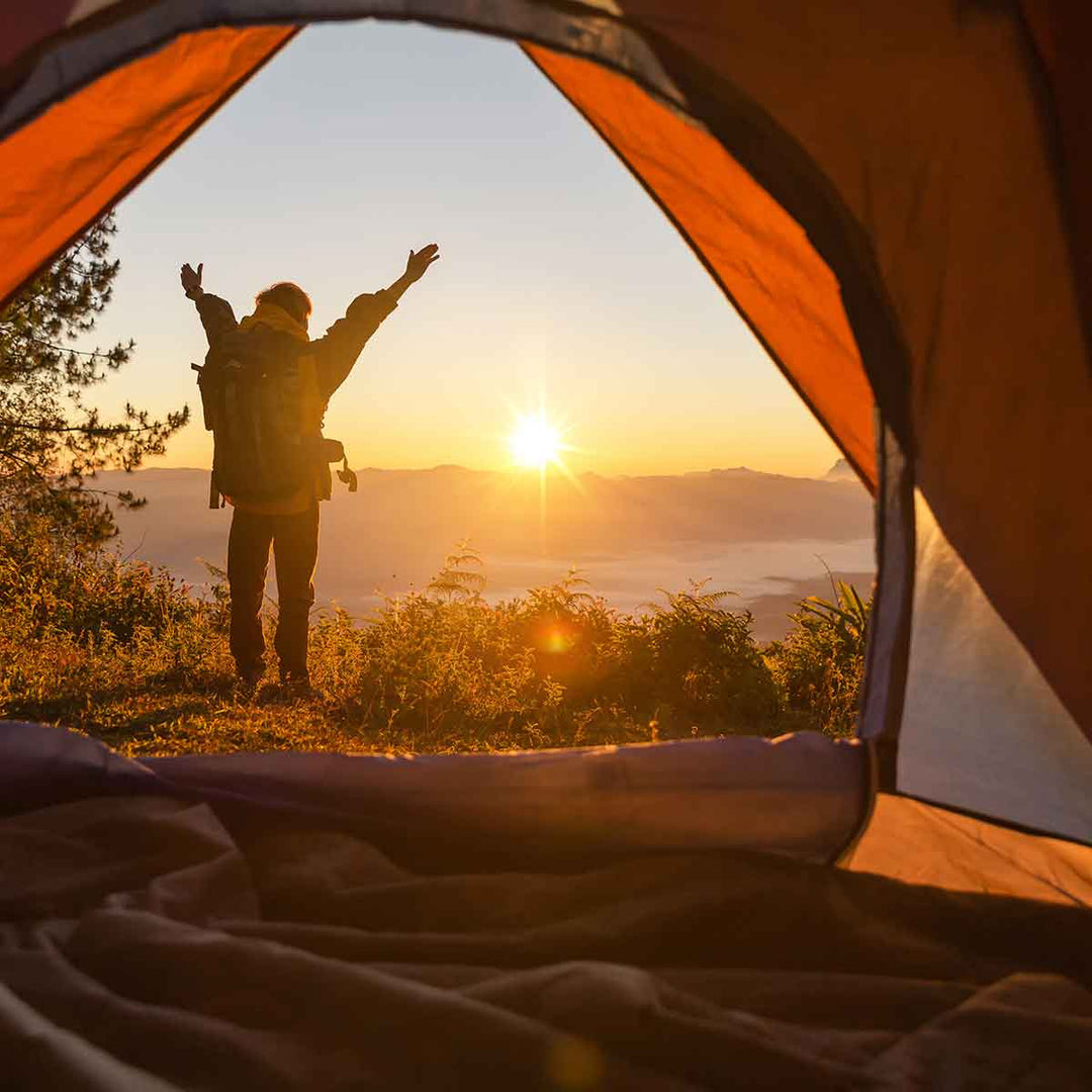 Person enjoying sunrise view from inside a camping tent, symbolizing outdoor personal hygiene and well-being.