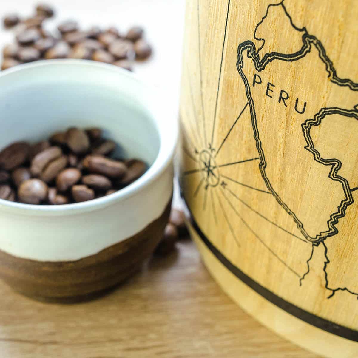 Close-up of a wooden container with a map of Peru and a cup filled with coffee beans.