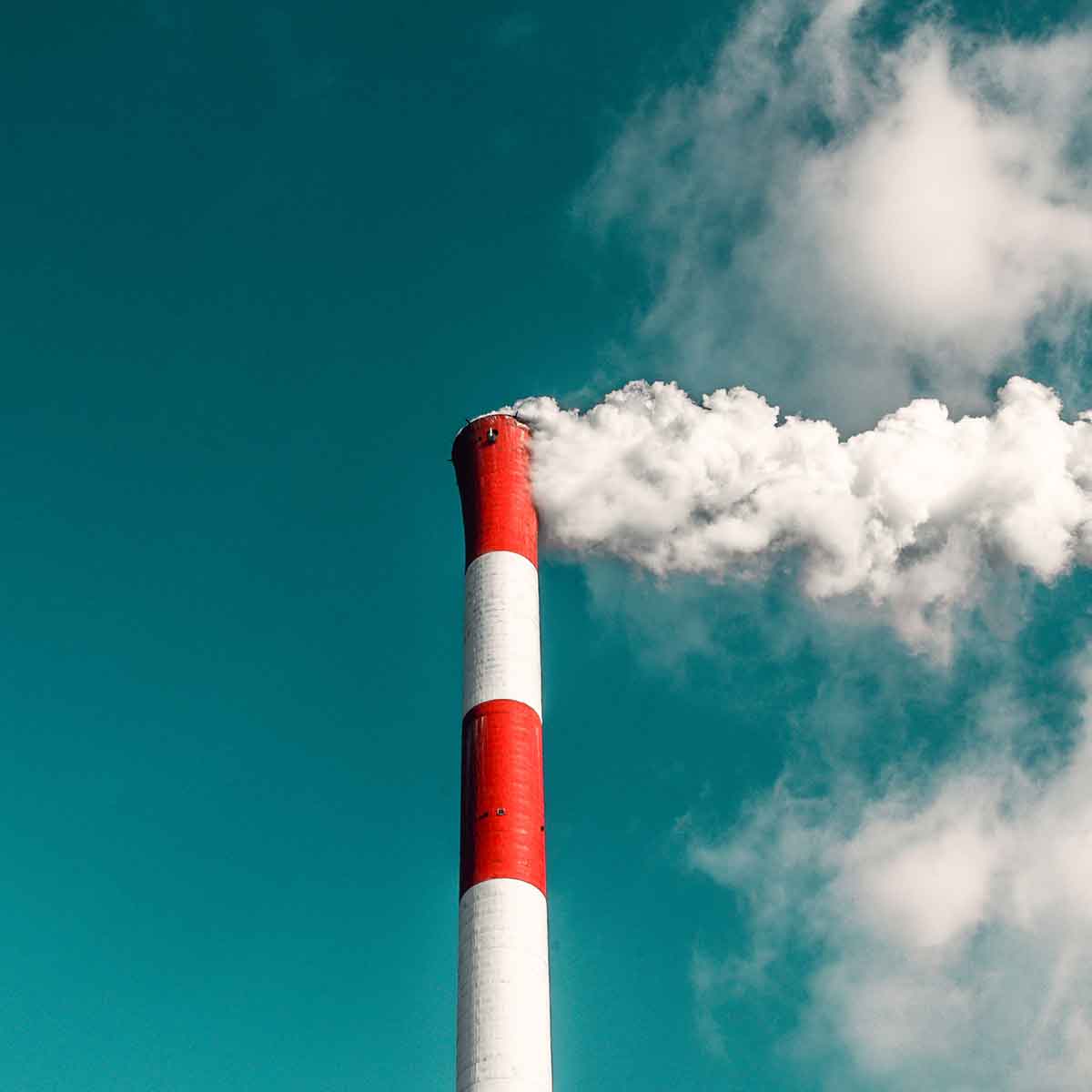 Industrial smokestack emitting white smoke against a clear blue sky, highlighting pollution issues affecting climate.