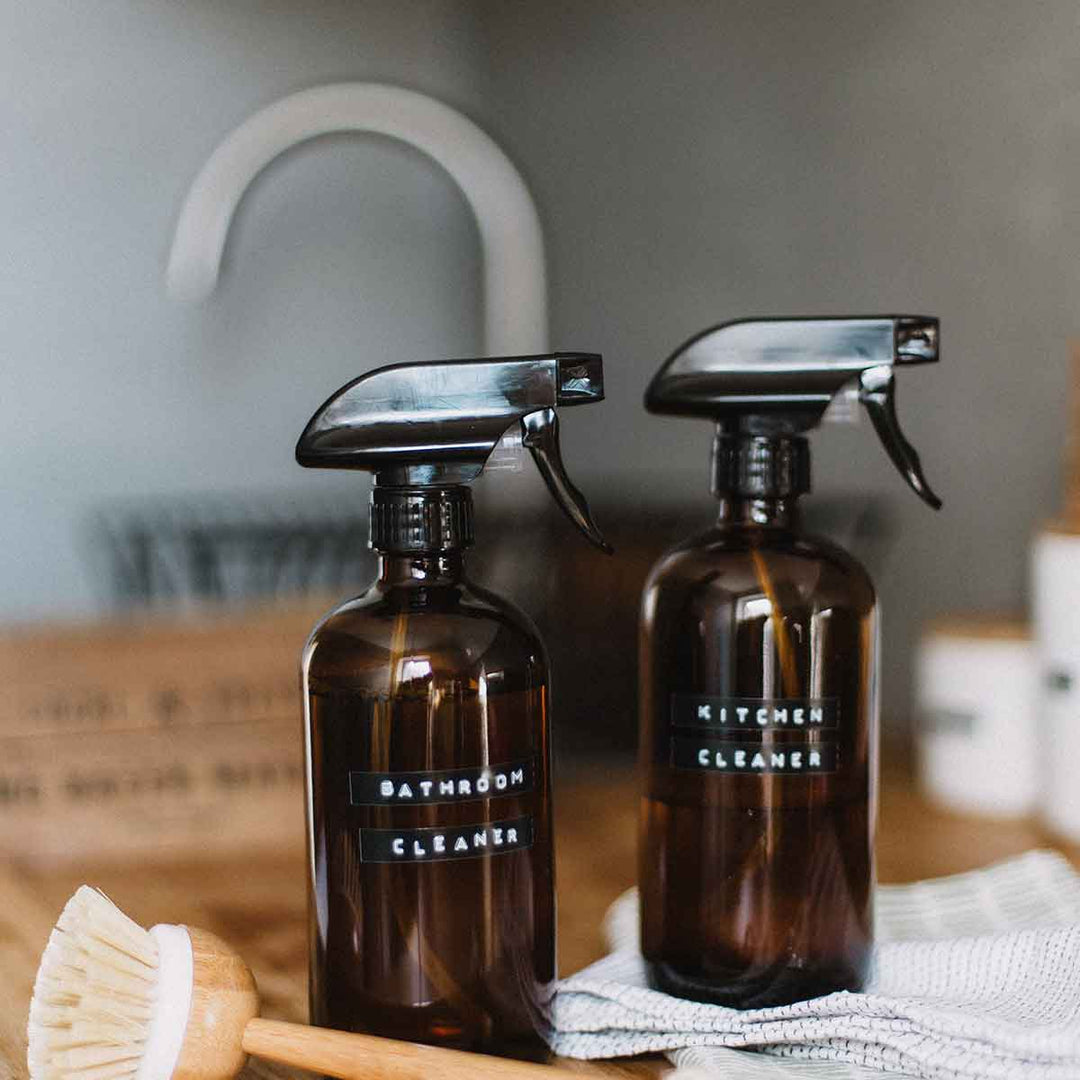Two spray bottles labeled Bathroom Cleaner and Kitchen Cleaner with a cleaning brush and cloth.