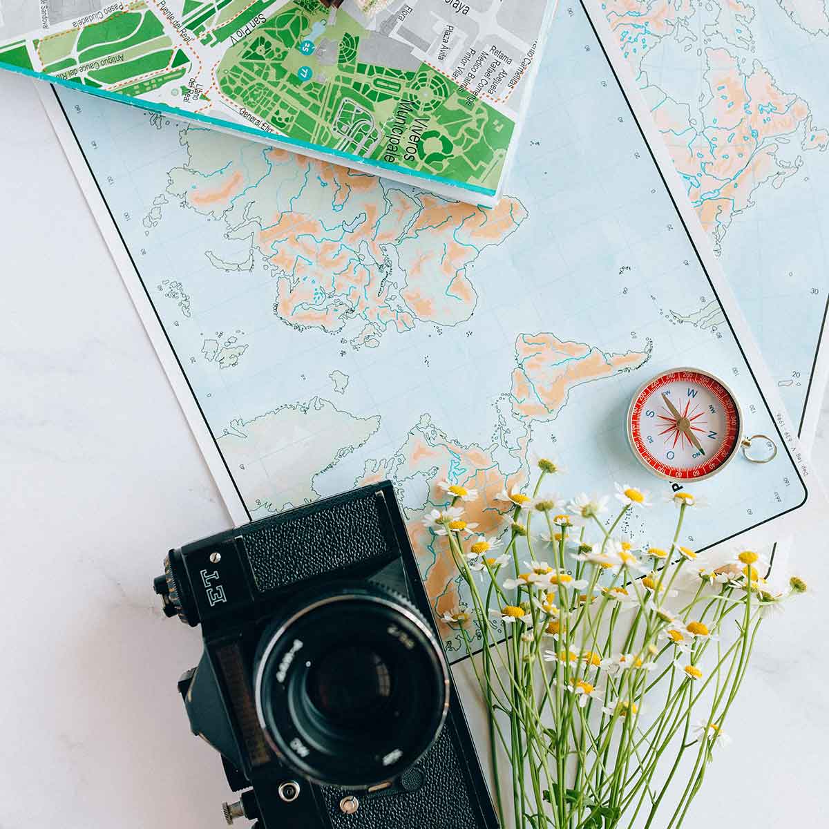 A vintage camera, compass, and maps arranged on a table with wildflowers, symbolizing travel and adventure.