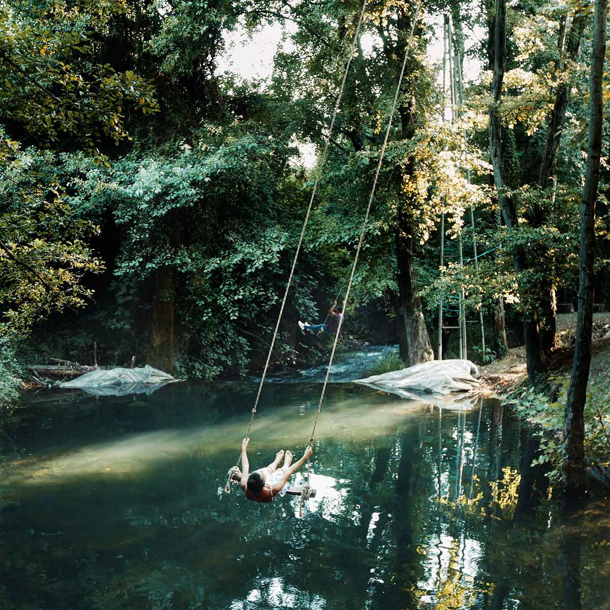 Person swinging over a tranquil river surrounded by lush greenery and trees.