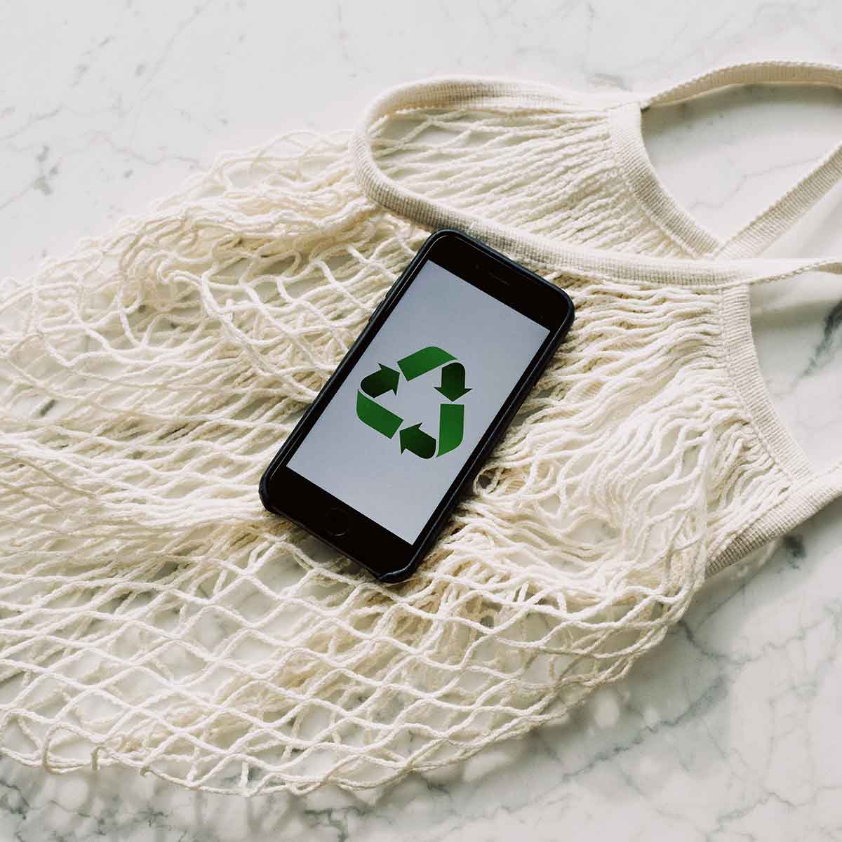 Smartphone displaying recycling symbol on a mesh tote bag, promoting eco-friendly practices.