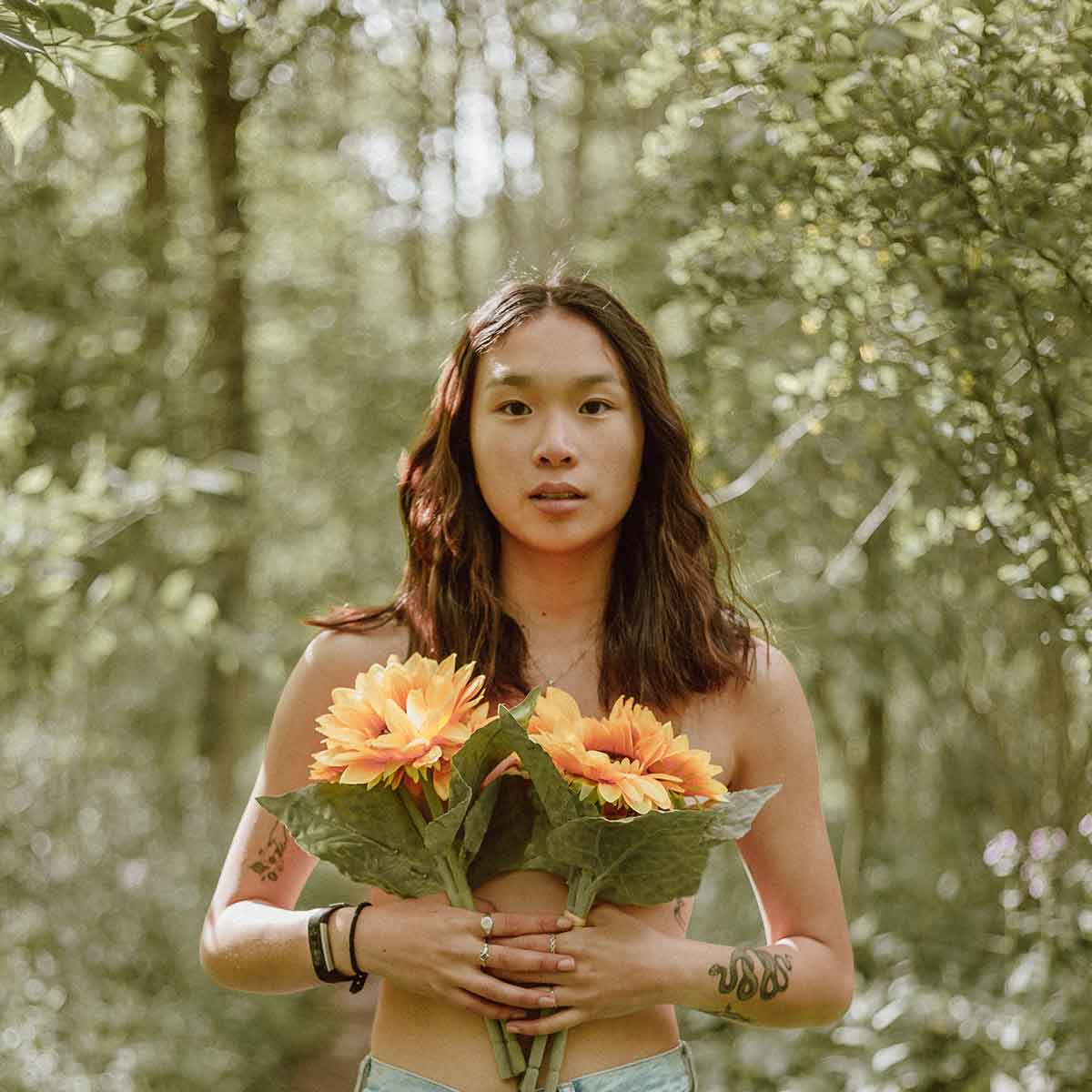 A person holding bright sunflowers in a forest, symbolizing natural beauty and connection to nature.