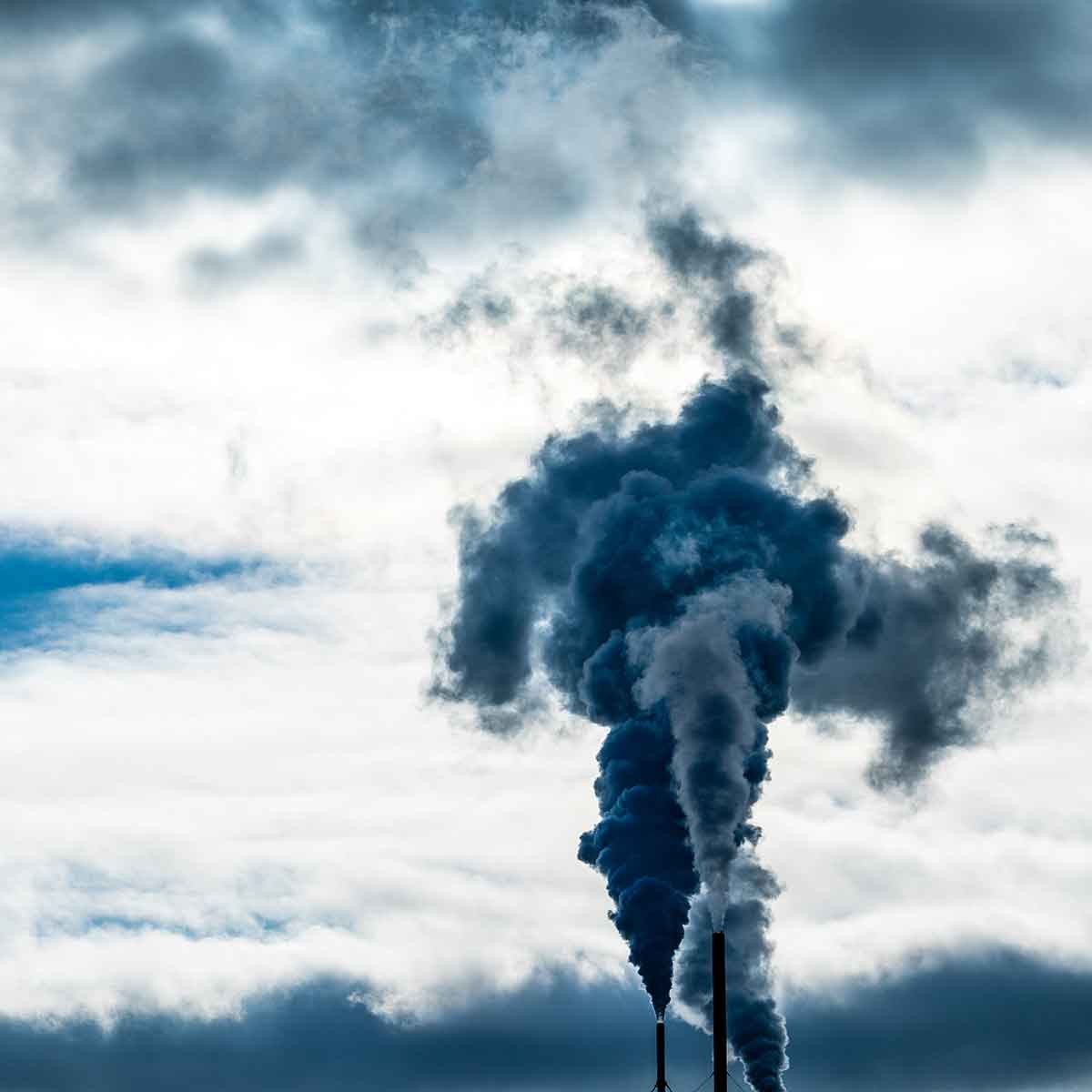 Dark smoke billowing from industrial chimneys into a cloudy sky, illustrating air pollution issues.