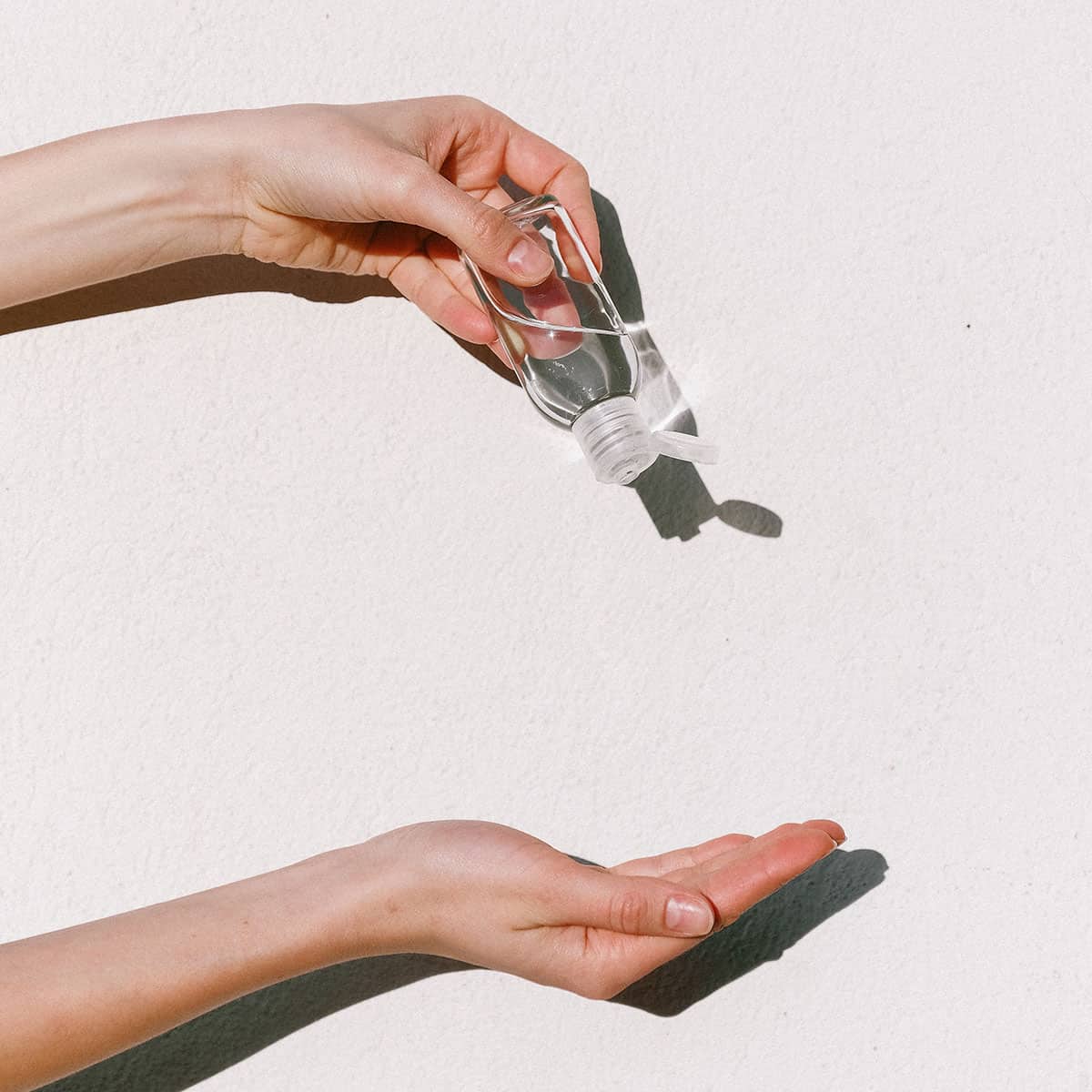 Person pouring a liquid from a bottle into their palm against a white background.
