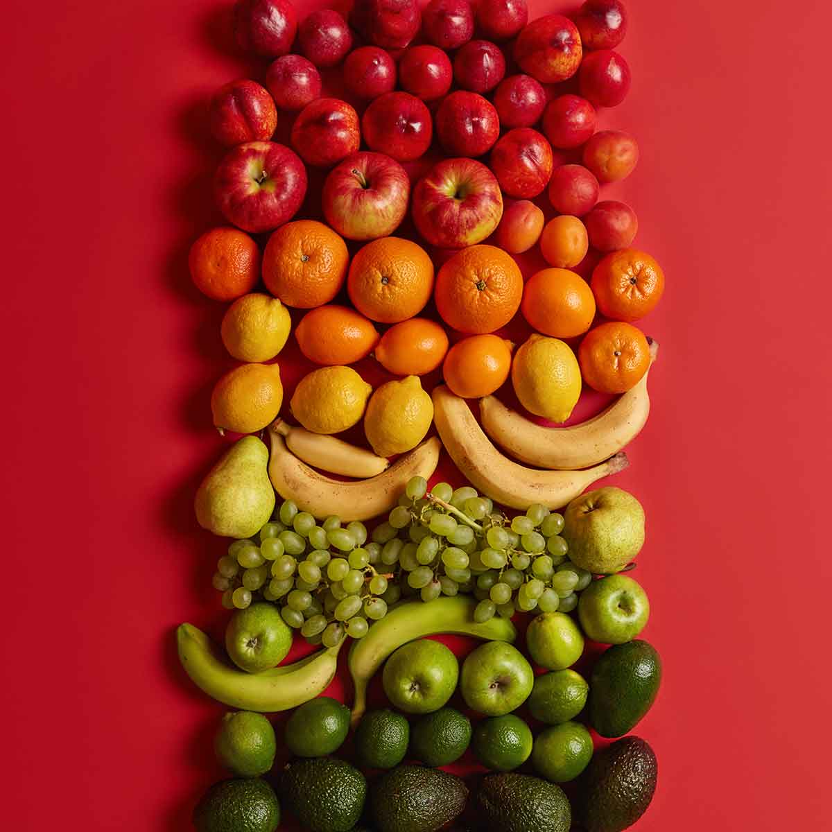 Colorful arrangement of various fruits including apples, oranges, bananas, and grapes on a vibrant red background.