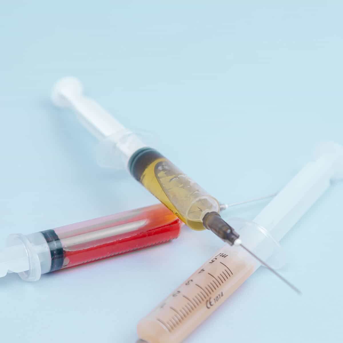 Used syringes filled with various colored liquids on a light blue background, representing medical waste.