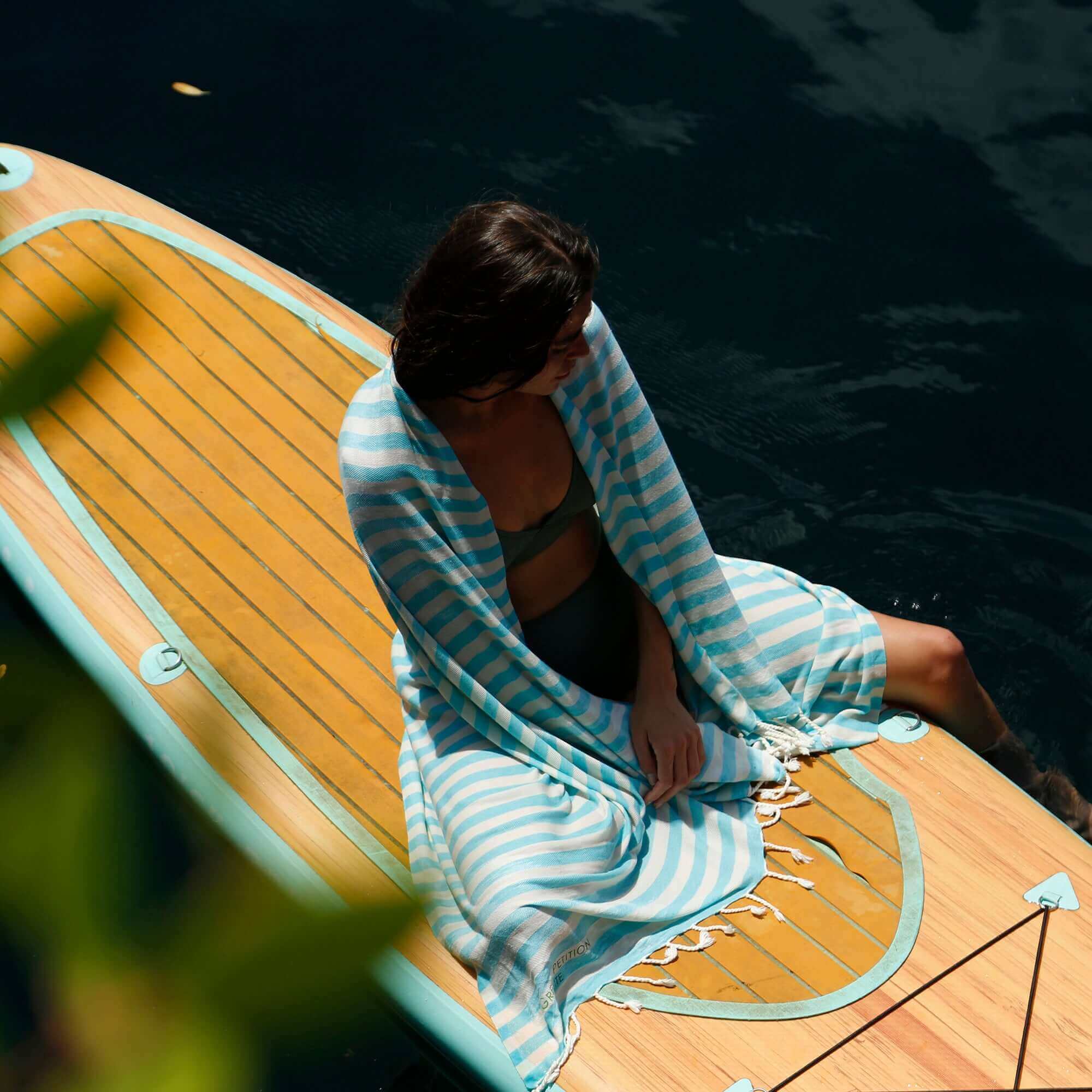 Model on paddle board wrapped in the Mare Capri Peshtemal towel, showcasing its soft organic cotton and striped design.