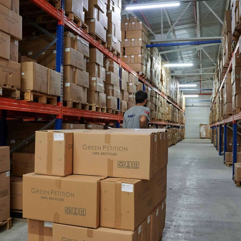 GREEN PETITON Warehouse aisle filled with stacked boxes and a worker organizing inventory.