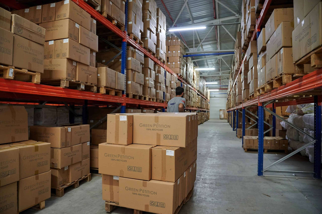 Warehouse aisle filled with stacked boxes and a worker organizing inventory.