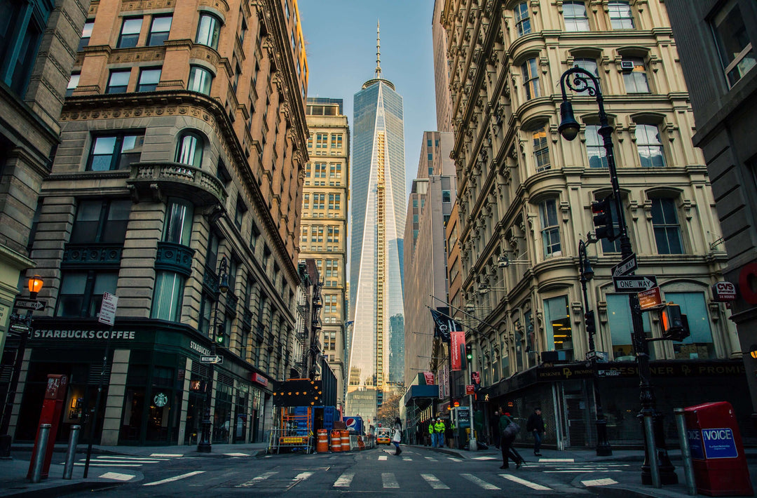 View of One World Trade Center framed by historic buildings on a New York City street, featuring urban architecture.