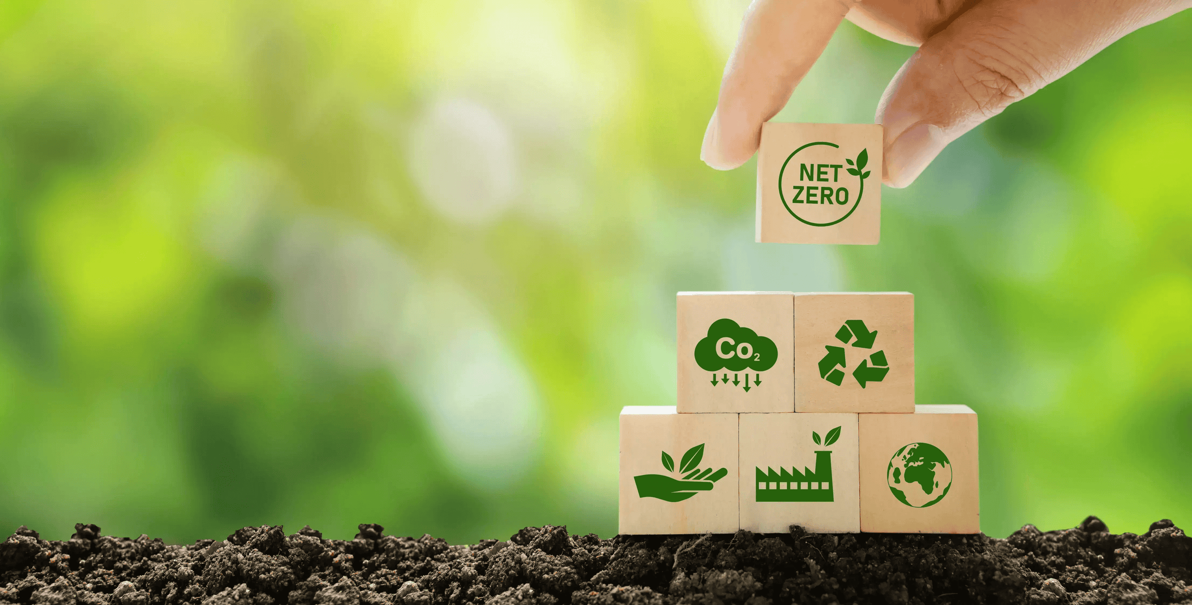 A hand places a block labeled 'NET ZERO' atop sustainability-themed blocks, symbolizing environmental responsibility.