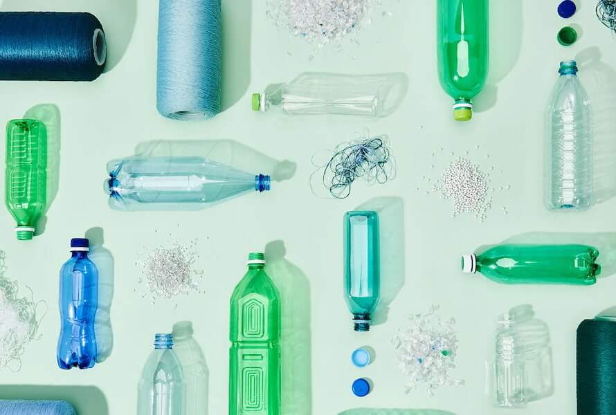 Colorful assortment of plastic bottles, spools of thread, and recycled materials on a light green background.