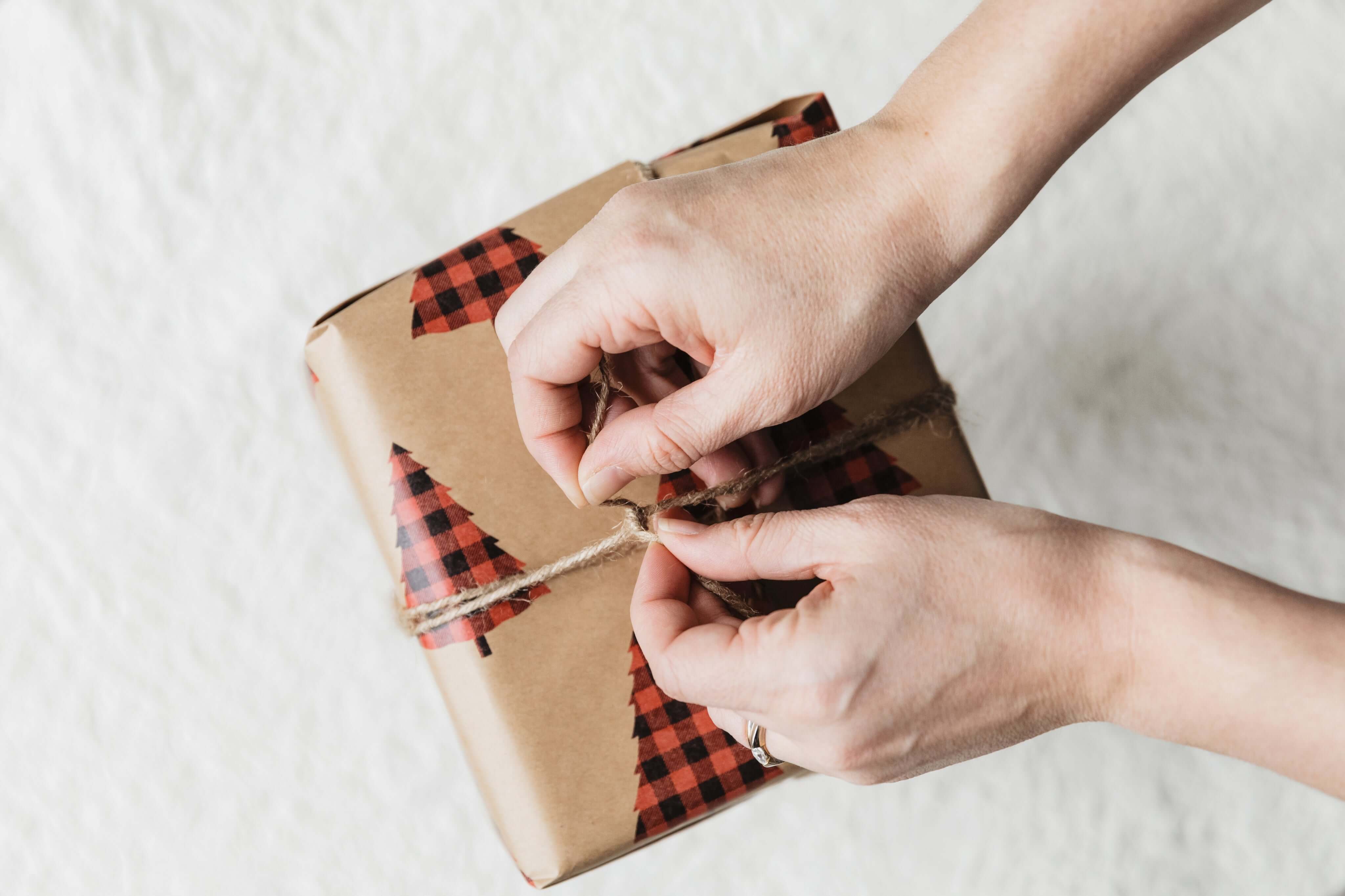 Hands tying a twine bow on a beautifully wrapped gift with plaid decoration.
