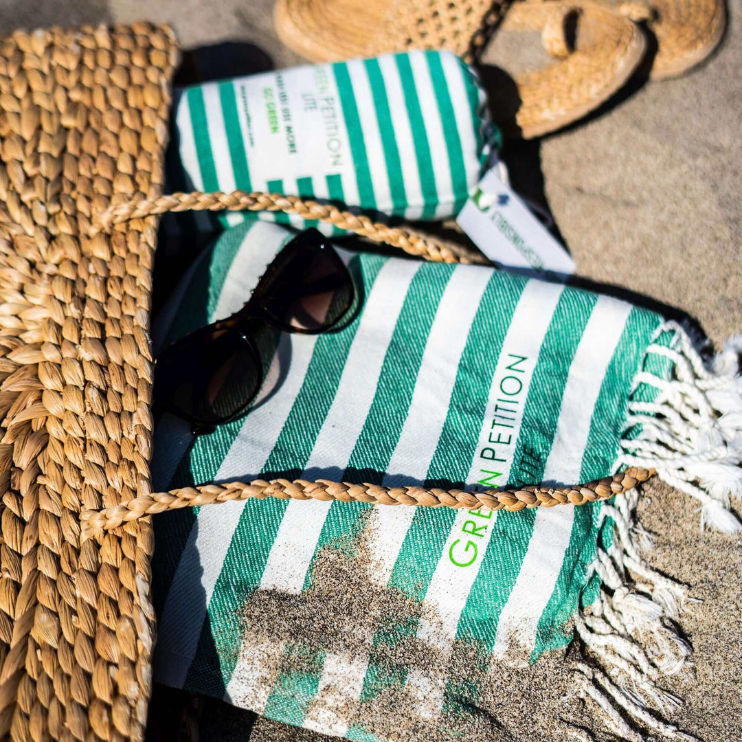 Mare Lime Peshtemal towel with striped design, sunglasses, and woven hat on sandy beach background.