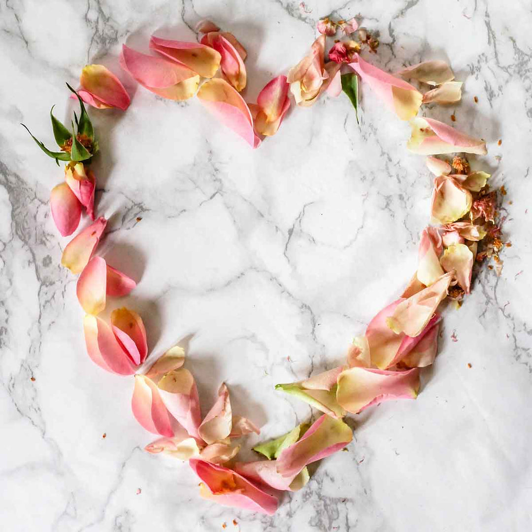 Heart-shaped arrangement of pink rose petals on a marble surface, symbolizing love and sustainability.