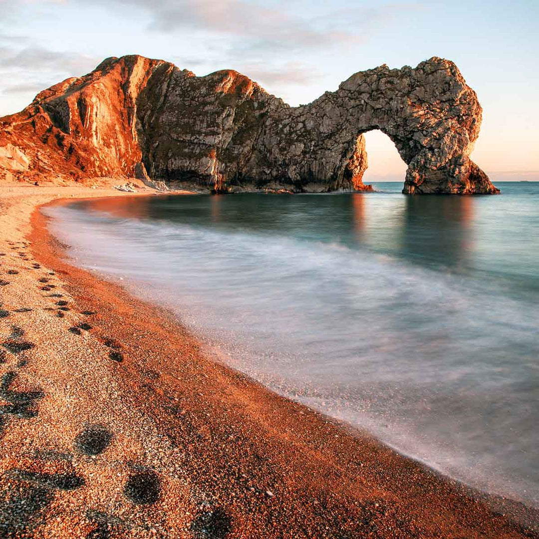 Scenic view of Durdle Door rock formation at sunset on a sandy beach in Europe.