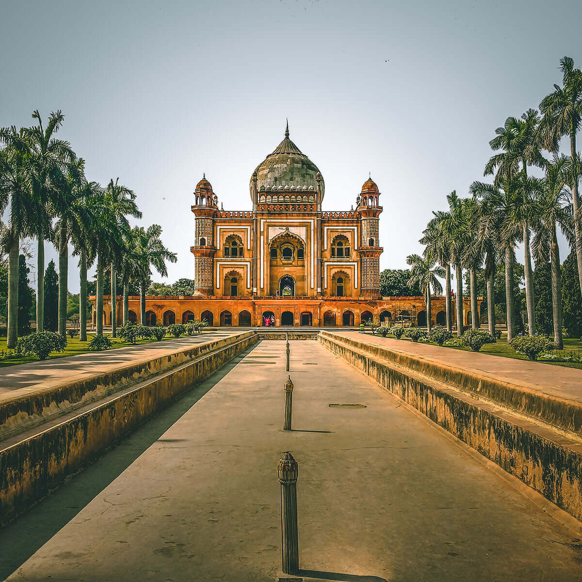 Historic Indian monument surrounded by palm trees and gardens, showcasing India's rich architectural heritage.