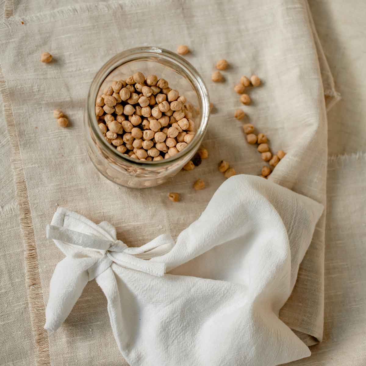 Glass jar filled with chickpeas on a linen cloth, highlighting sustainable kitchen practices.