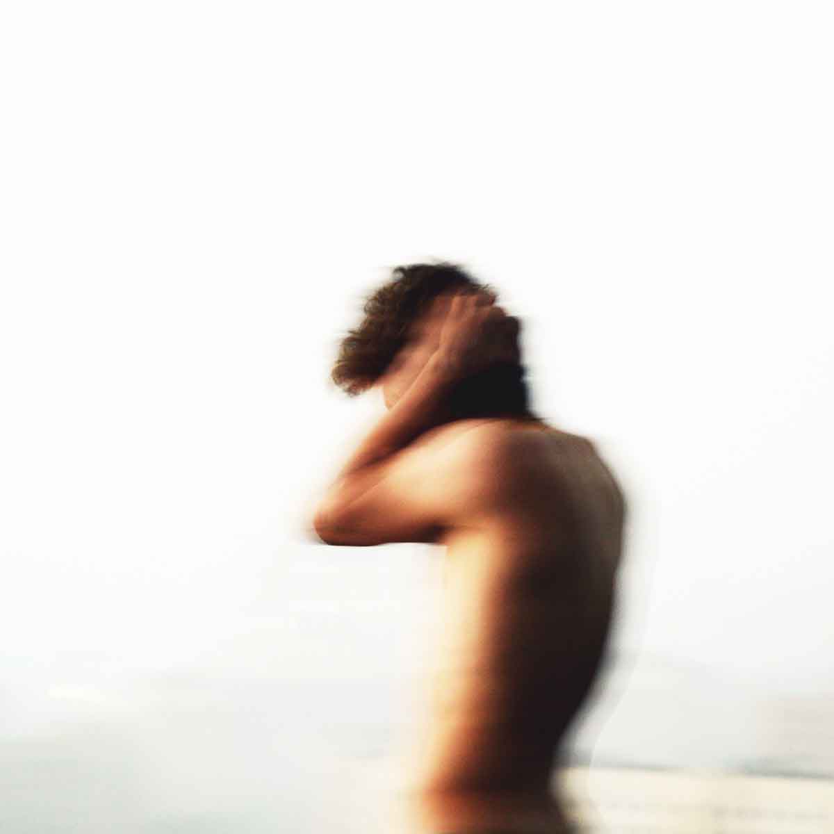 A blurred figure of a person holding their head, expressing distress or discomfort against a pale backdrop.