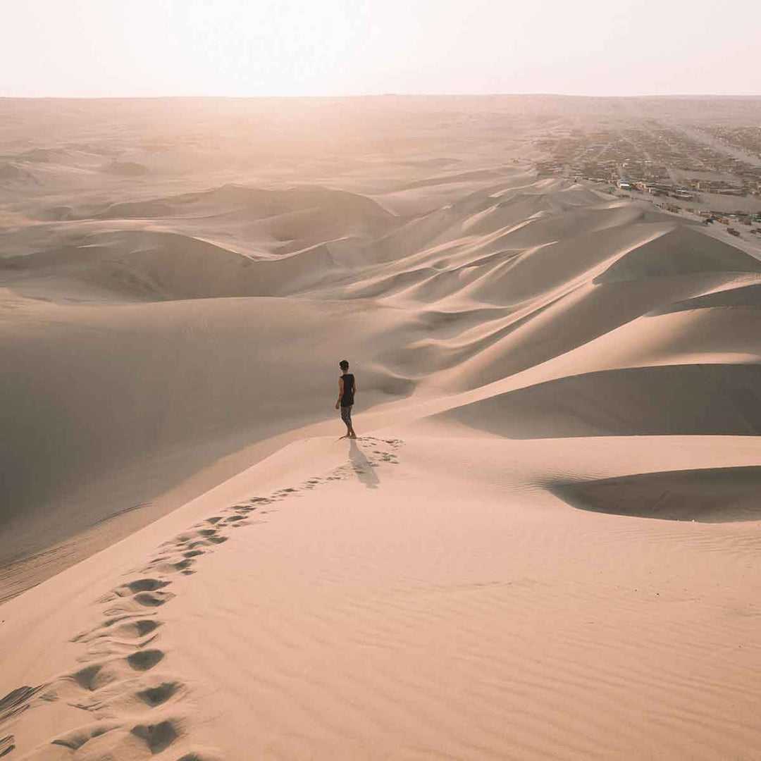 A lone figure standing on sand dunes during sunset, illustrating the vastness of natural landscapes.