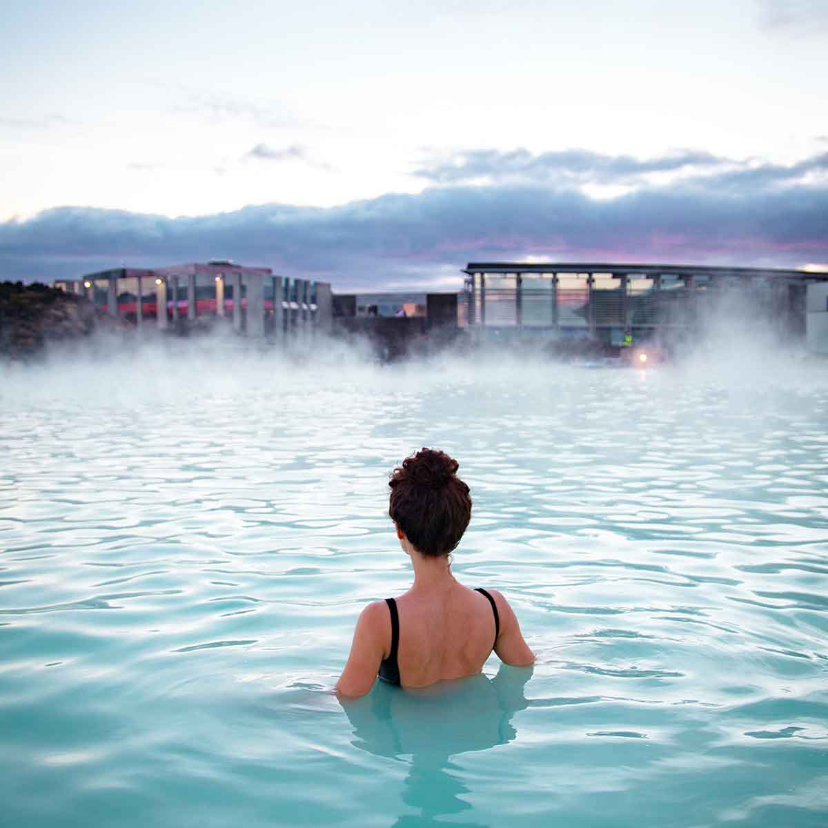Woman relaxing in a serene thermal spa with mist rising in a tranquil setting.
