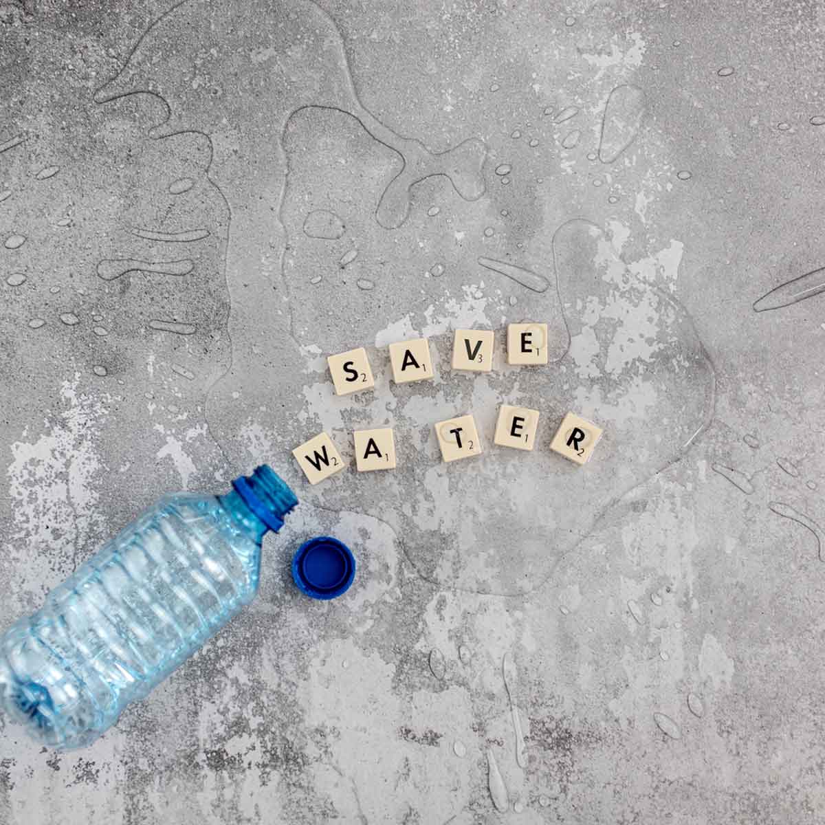 Plastic water bottle next to wooden tiles spelling 'SAVE WATER' on a gray surface.