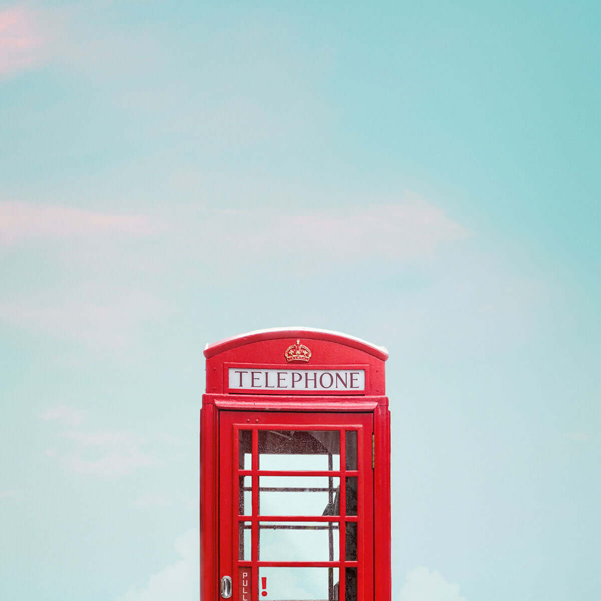 Classic red telephone booth against a clear blue sky, an iconic symbol of Britain.