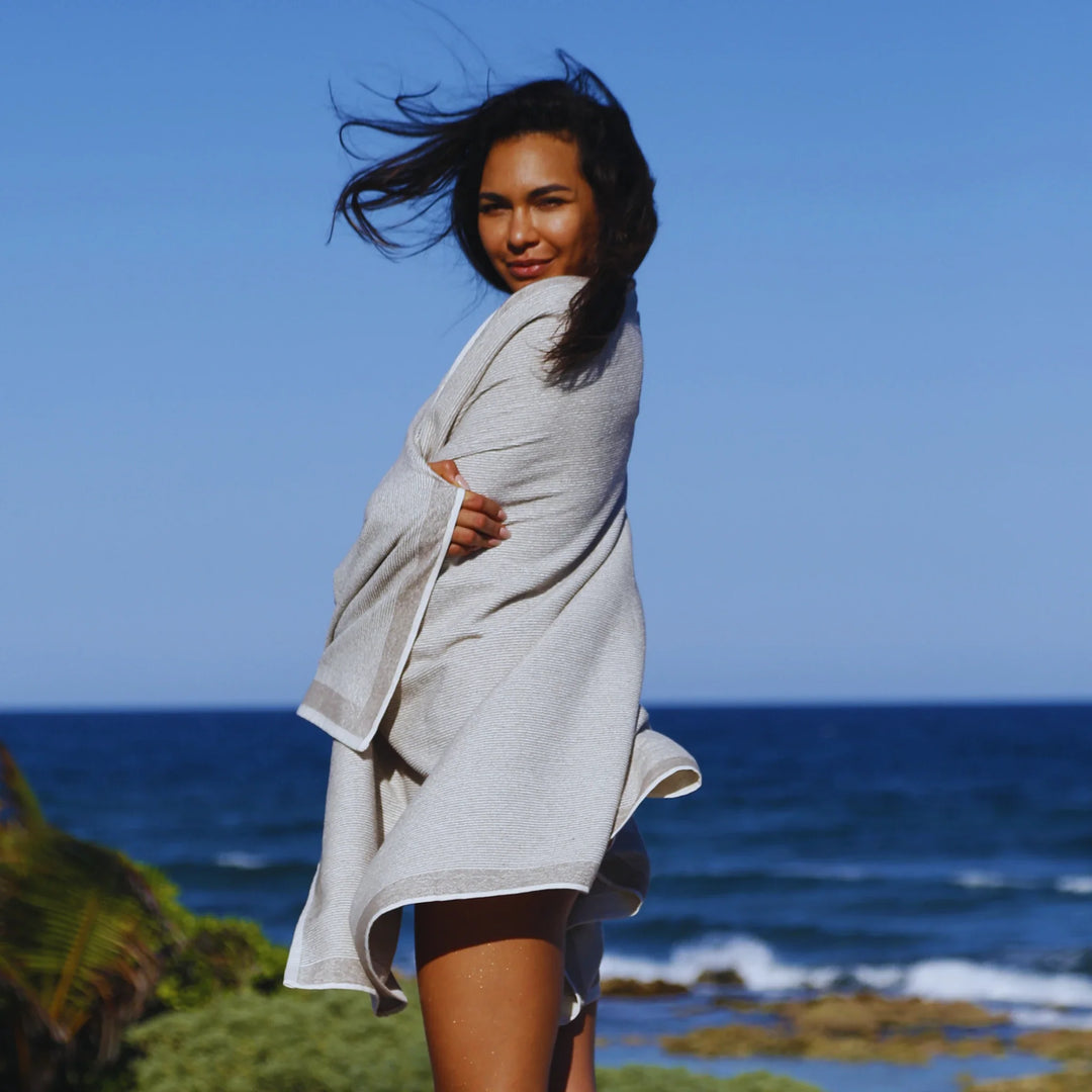 Woman wrapped in a cozy gray blanket, exuding a calm vibe on a sunny day near white chairs.