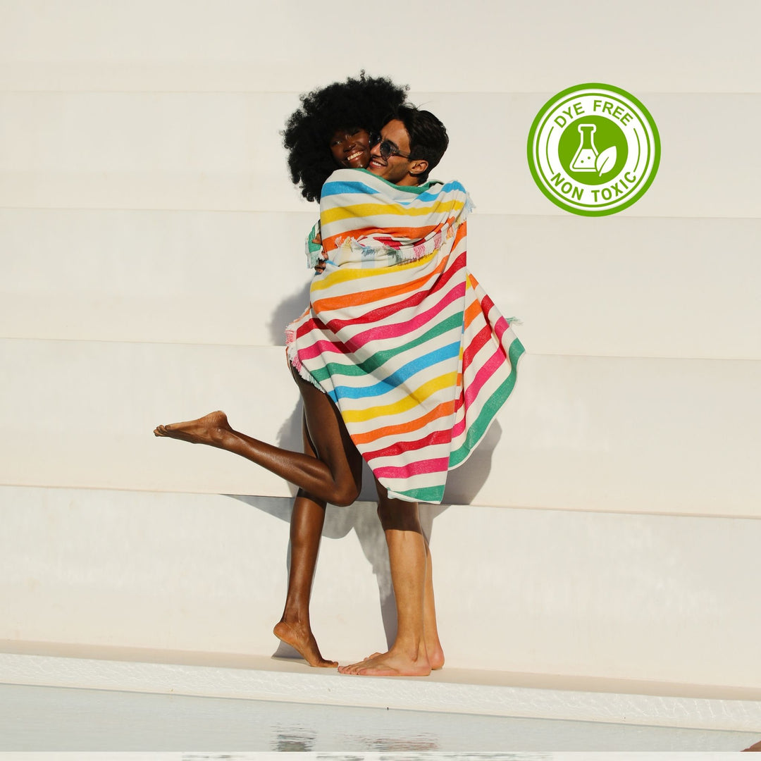 A colcored beautful woman who has fluffy curly hair and hugg the her boy frend. Both of them has wrapped in a colorful striped Green Petition 100% Recycled towel with a 'Dye Free' and 'Non Toxic' logo on a light background.