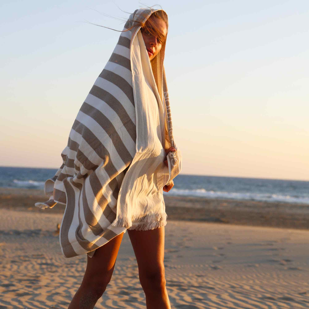 Woman on a beach with a striped Green Petition Delmor Sand Beige towel draped over her head