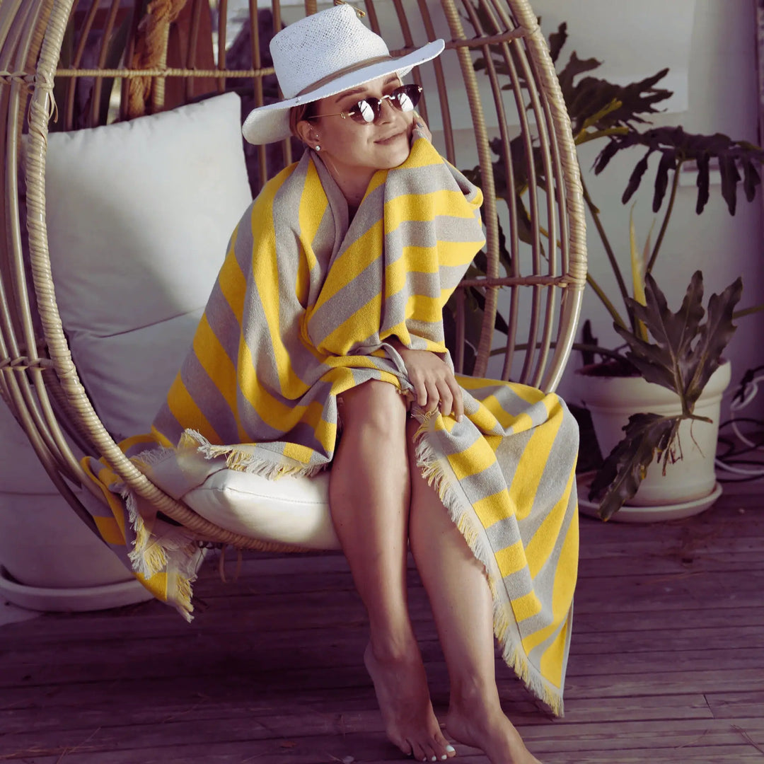 Woman wrapped in a yellow and gray striped "Green Petition Maris Amber" towel sitting in a hanging chair.