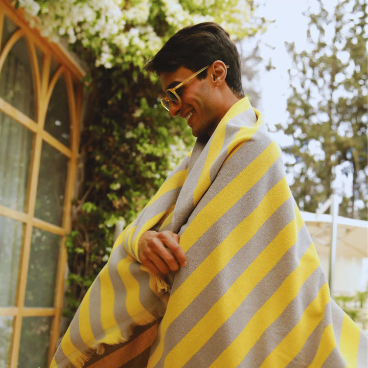 Person wrapped in a yellow and gray striped "Green Petition Maris Amber" blanket outdoors