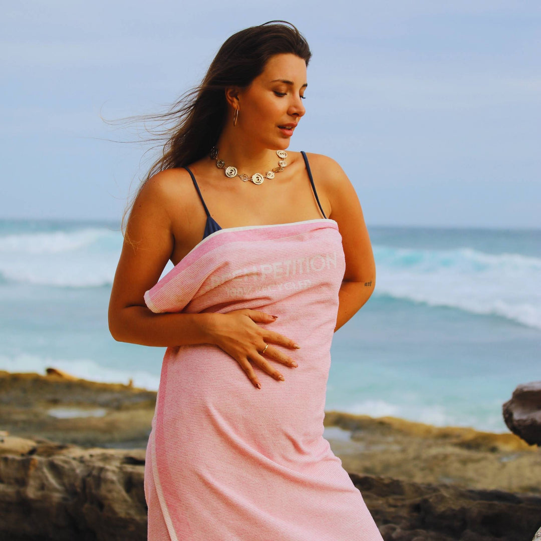 Woman holding a pink towel with 'Green Petition' branding on a beach.