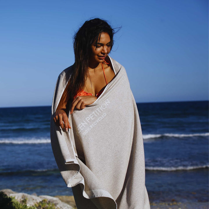 Woman wrapped in a  Green Petition CALM clay towel on a beach with ocean in the background