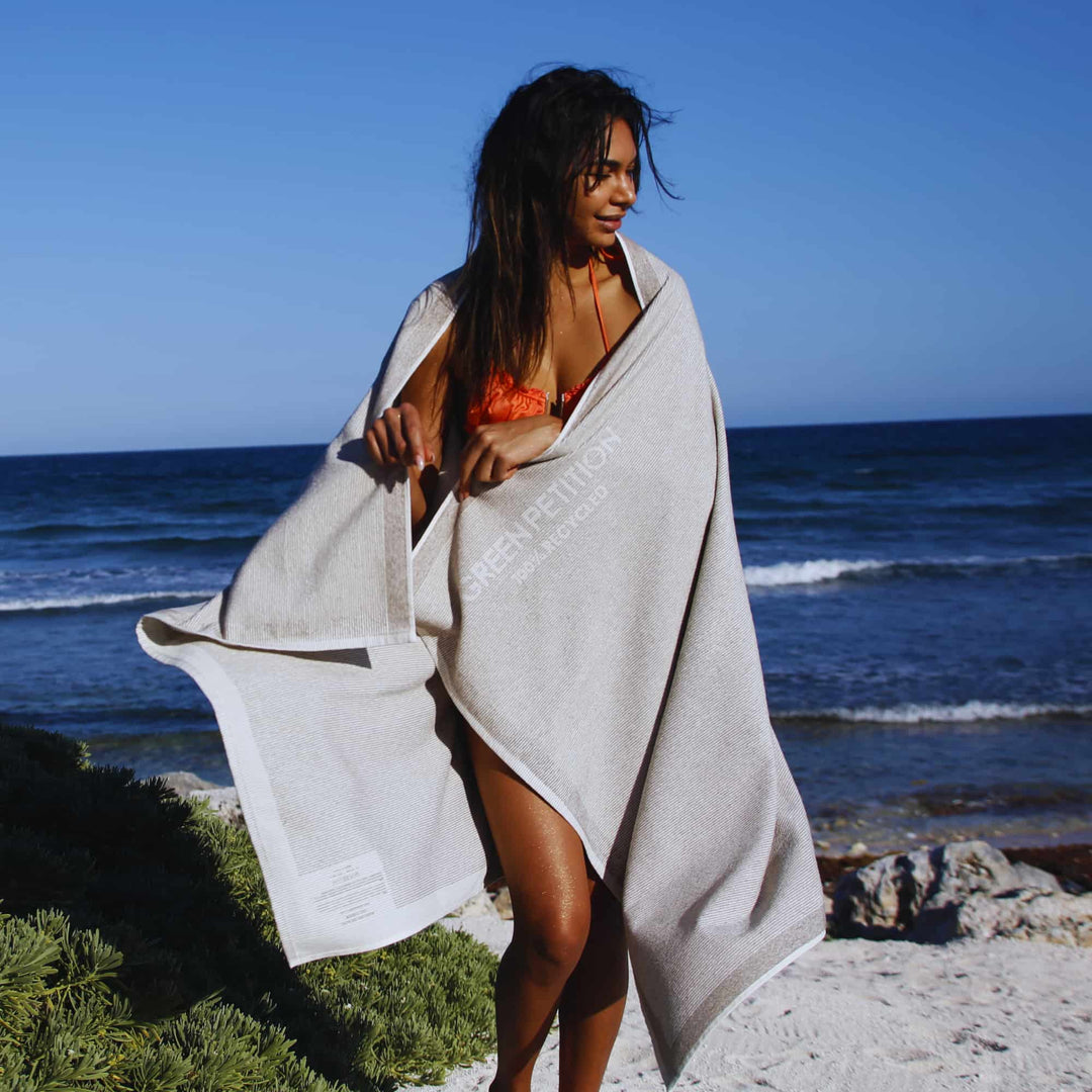 Woman wrapped in a Green Petition CALM clay towel on a beach with ocean in the background