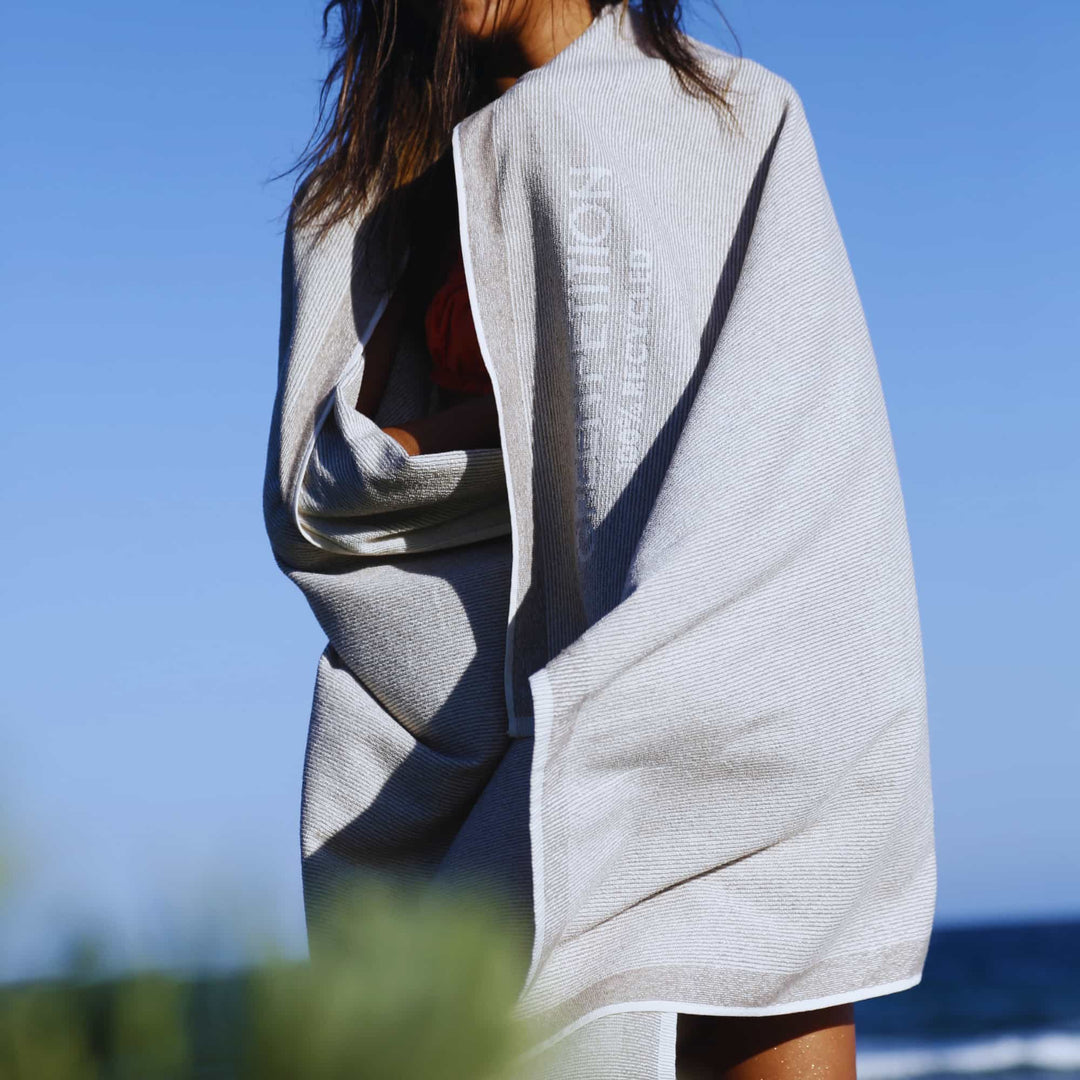 Woman wearing a Green Petition CALM clay towel with branding against a clear blue sky