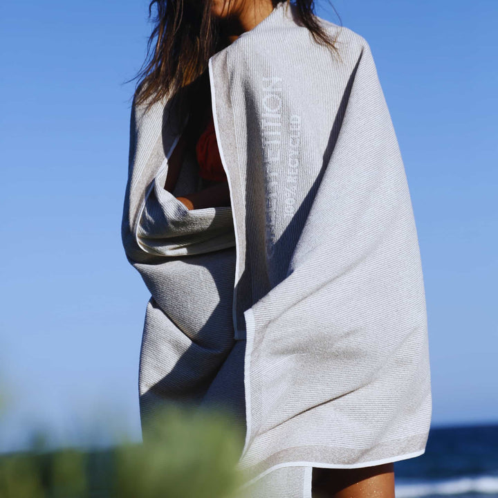Woman wearing a Green Petition CALM clay towel with branding against a clear blue sky