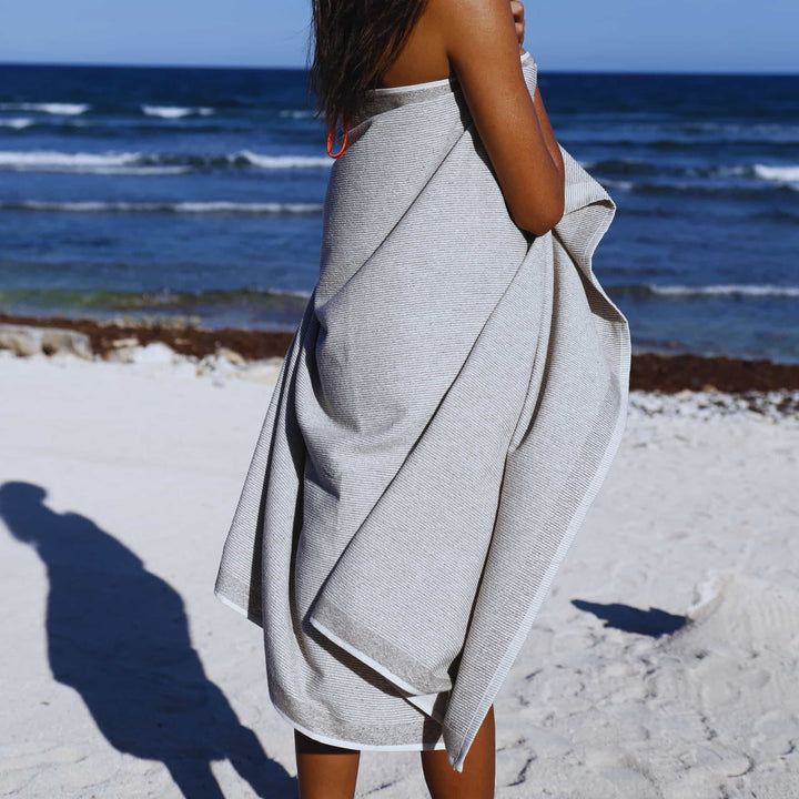 Woman wrapped in a gray towel on a beach with ocean in the background