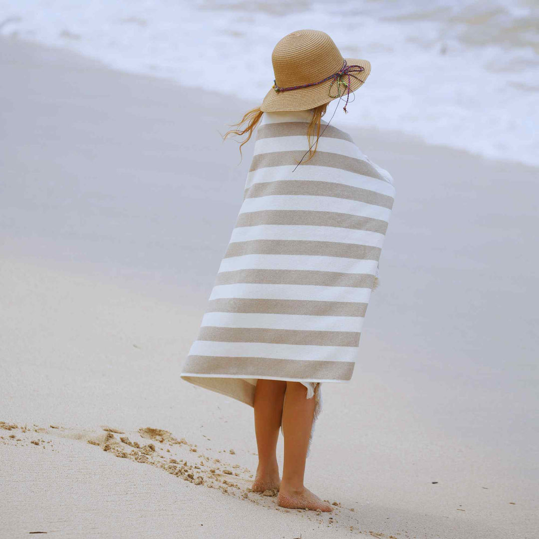 a kid wrapped in a striped Green Petition Delmor FIT Sand Beige towel on a beach
