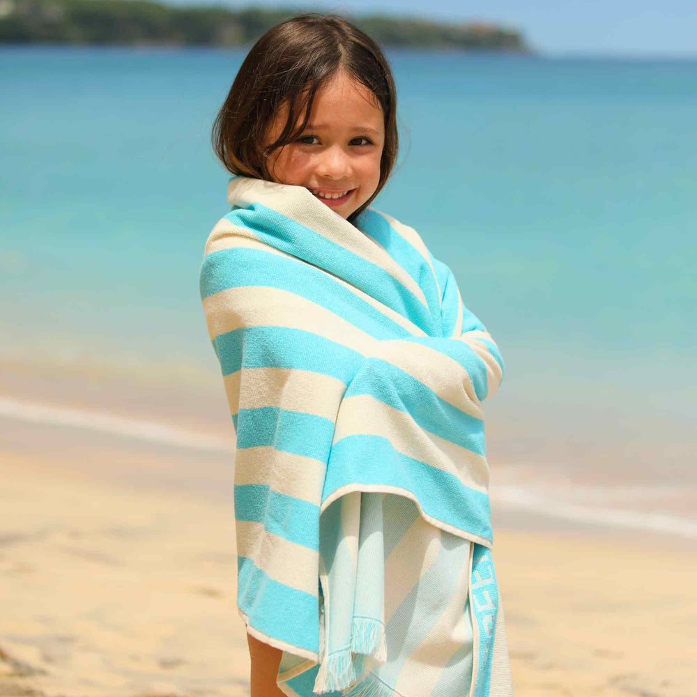 Child wrapped in a blue and white stripedGreen Petition Delmor Fit Capri  towel on a beach