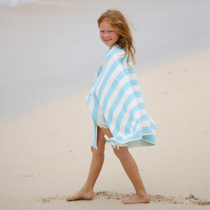 Child wrapped in a blue and white striped Green Petition Delmor Fit Capri  towel on a sandy beach