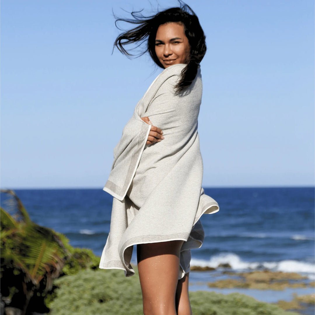 Woman wrapped in a Green Petition Calm Clay towel on a beach with ocean in the background