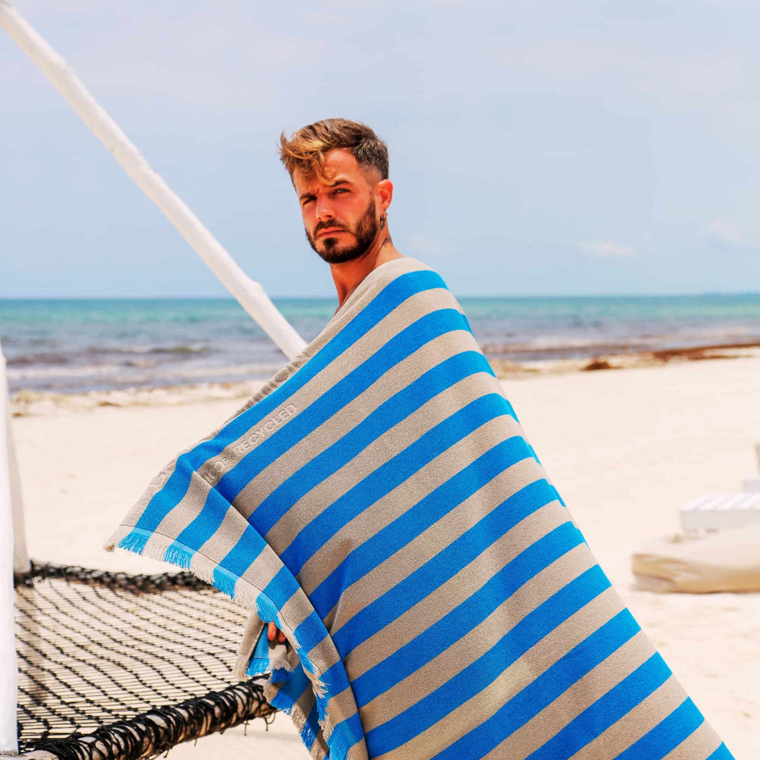 Man on a beach wrapped in a blue and white striped "Green Petition Maris Laguna" Beach Towel 