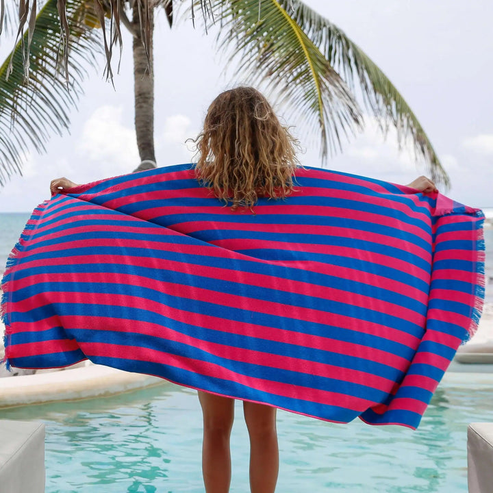 Person holding a red and blue striped towel by a pool with palm trees in the background